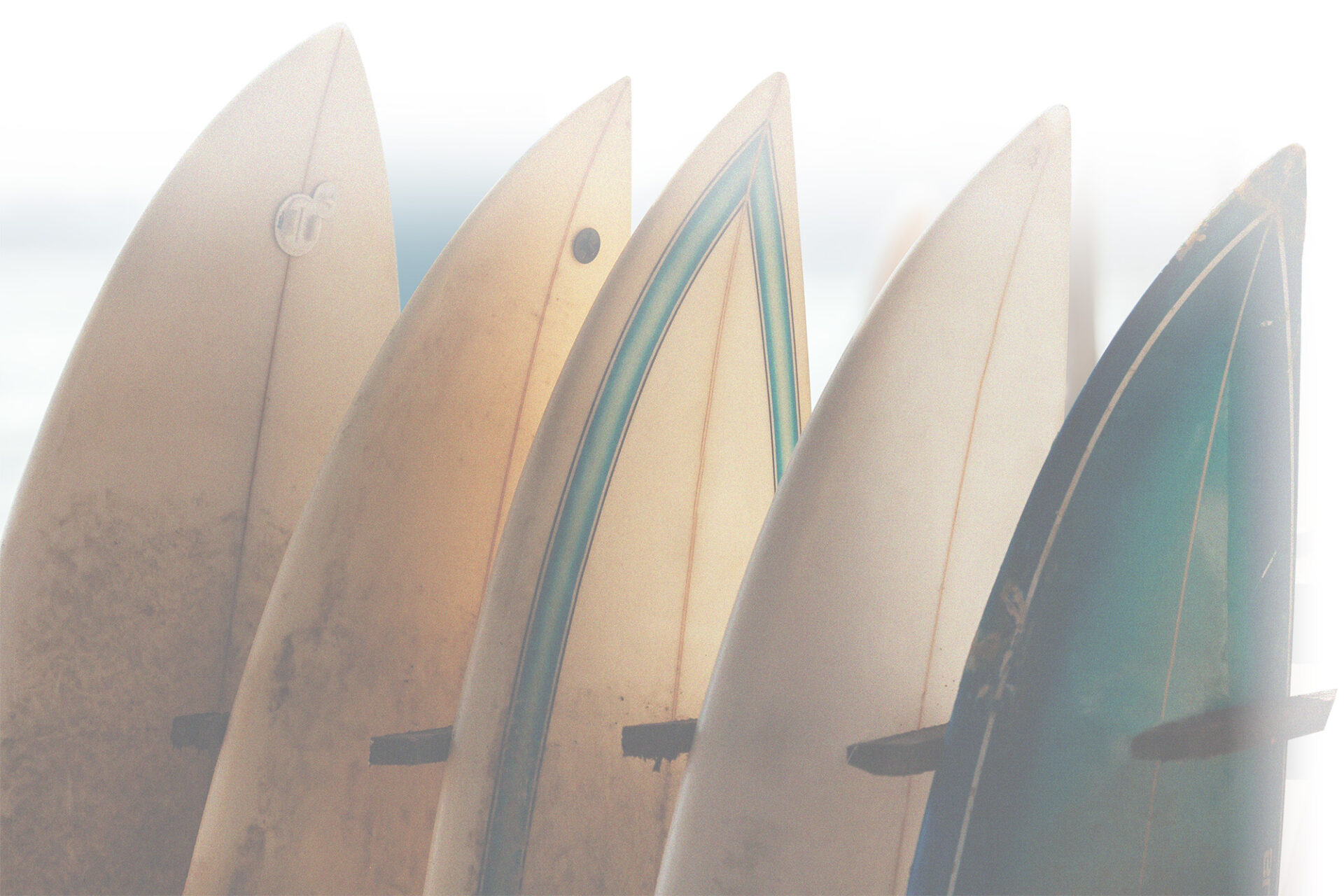 Set of different color surf boards in a stack by ocean.