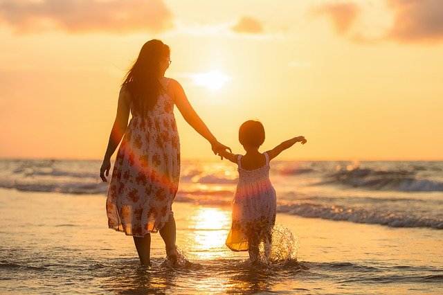 woman holding a little girls hand, walking in the surf