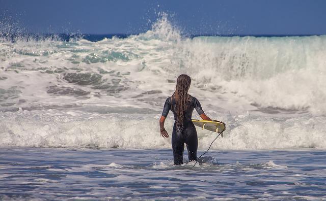 girl in a wetsuit holding a surfboard, walking out into the ocean